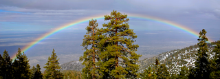 View from a mountaintop of a large rainbow with a valley in the background: A rainbow is caused by the sunlight shining through raindrops, spray or mist.